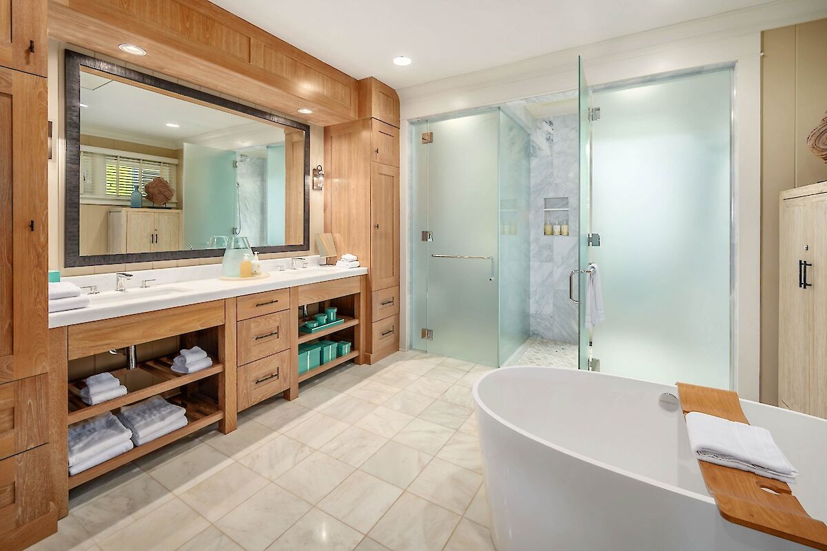 A modern hotel-style bathroom with a freestanding tub, glass-walled shower, wooden vanity area, big mirror, and neatly stacked towels.