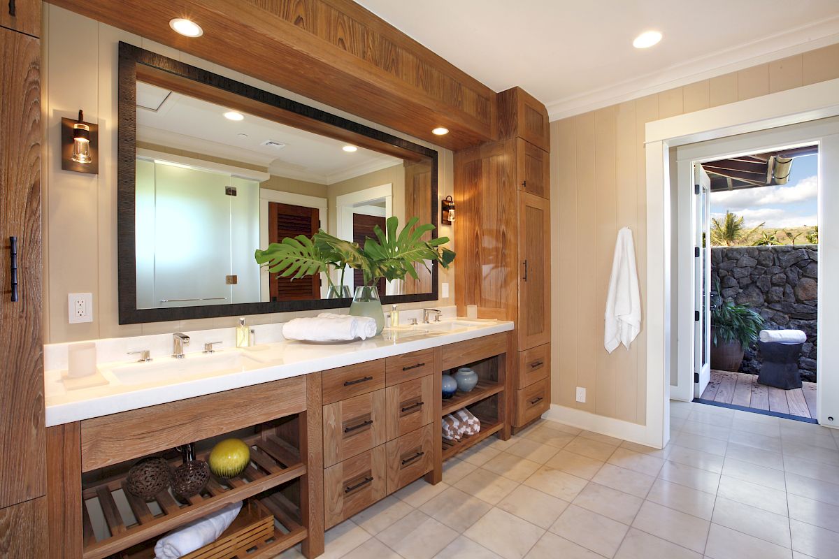 The image shows a modern bathroom featuring a wooden vanity, large mirror, plants, and access to an outdoor area.