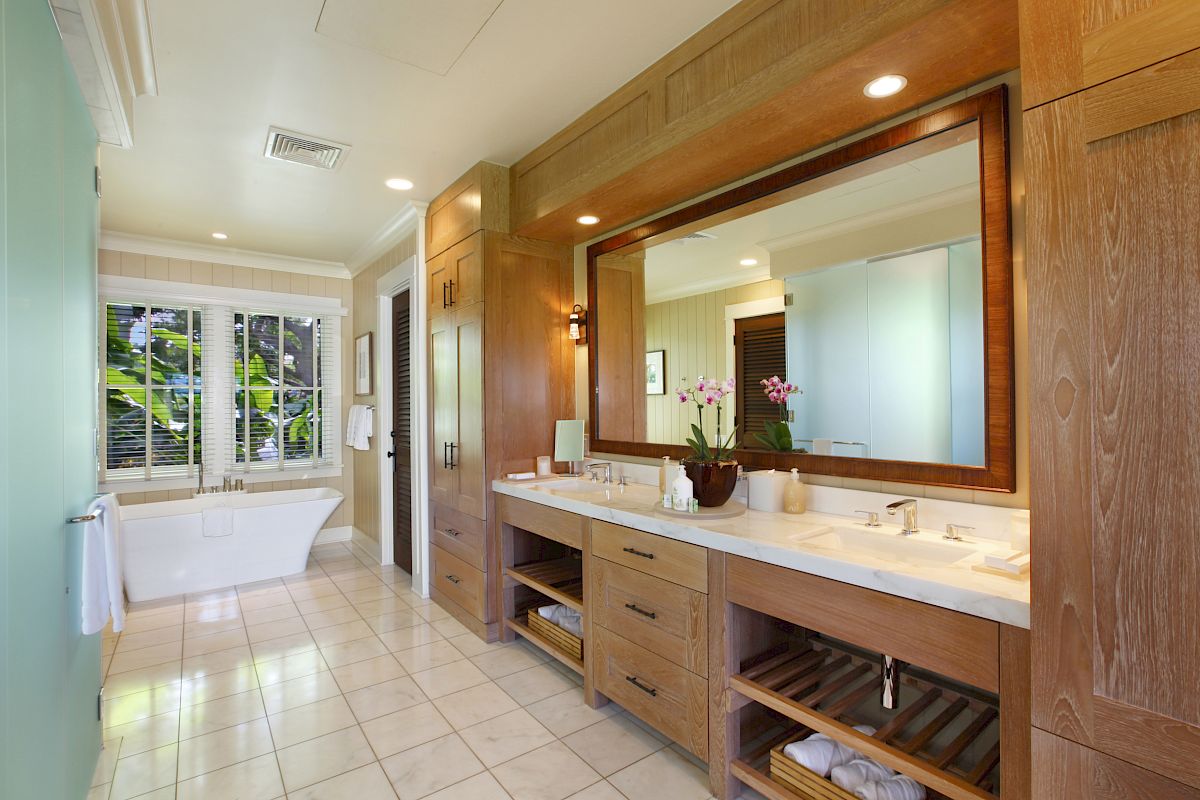 The image features a stylish bathroom with a large mirror, wooden cabinets, a soaking tub, and natural light from large windows.
