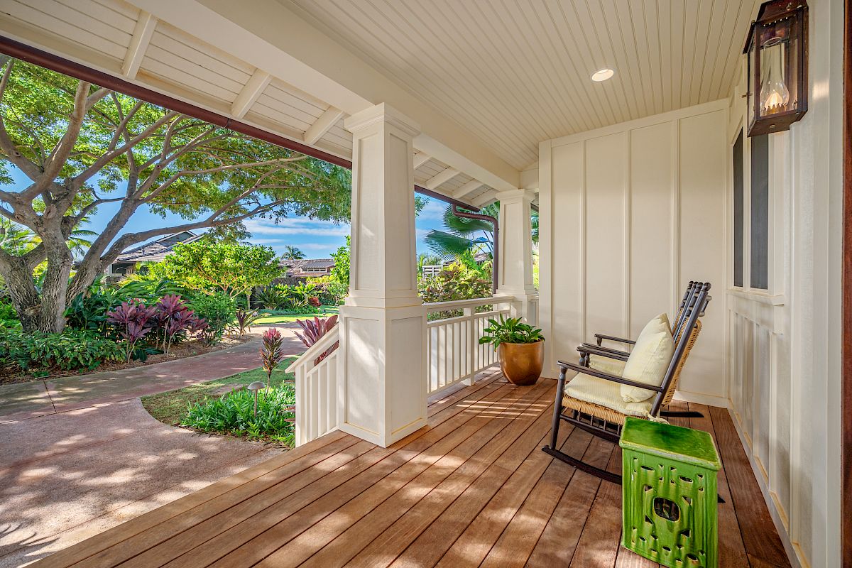 A charming porch with a rocking chair, green accents, and lush greenery outside creates a relaxing outdoor space.