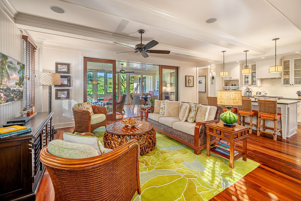 A cozy living room with wicker furniture, a vibrant green rug, and a view into a modern kitchen. It has large sliding glass doors.