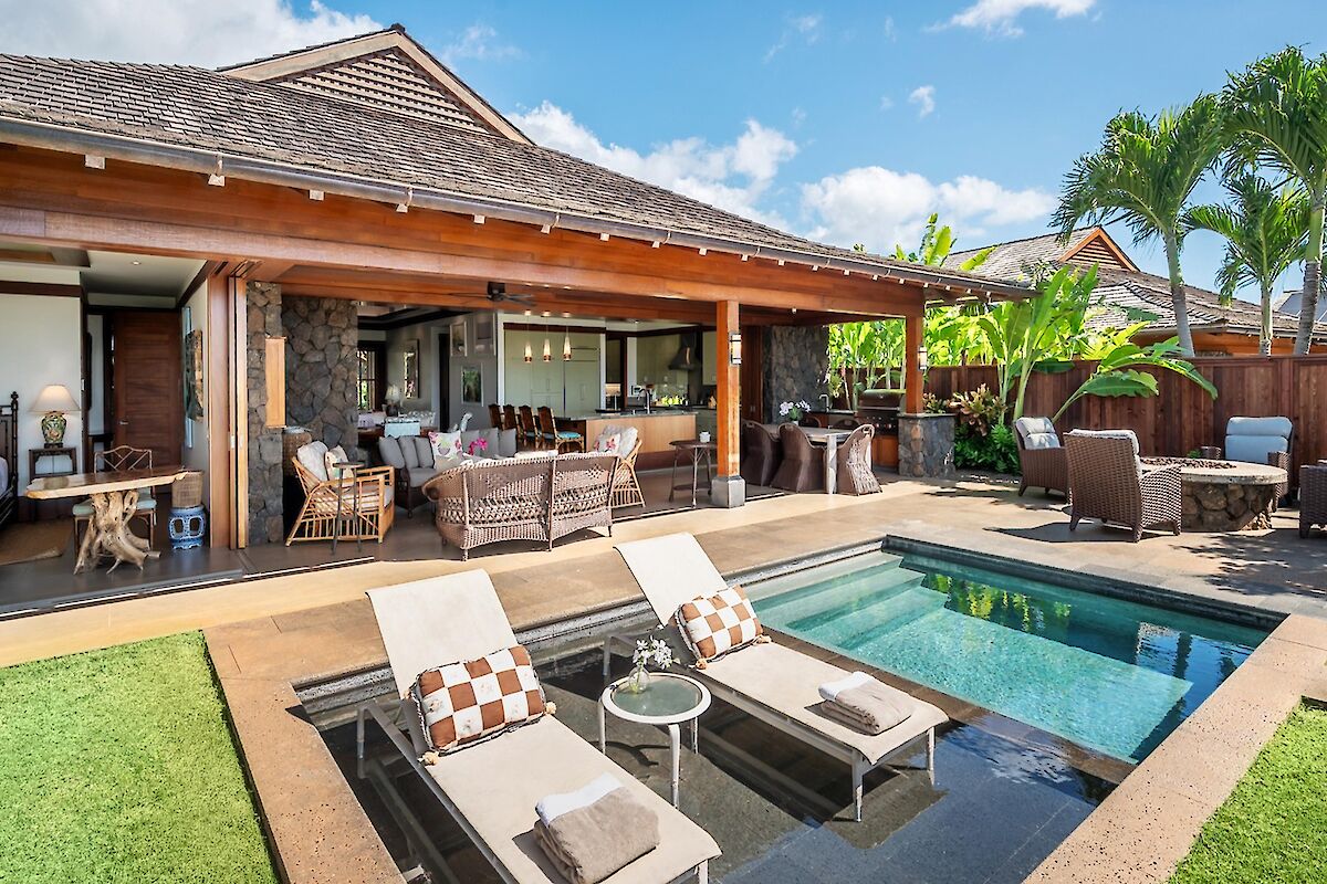 A sunny backyard with a modern patio, pool, sun loungers, and a cozy outdoor seating area by a stylish house, perfect for relaxing and entertaining.