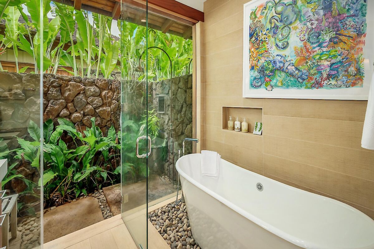 A modern glass-enclosed bathroom with a freestanding tub and a lush tropical garden view outside, plus a colorful abstract painting on the wall.