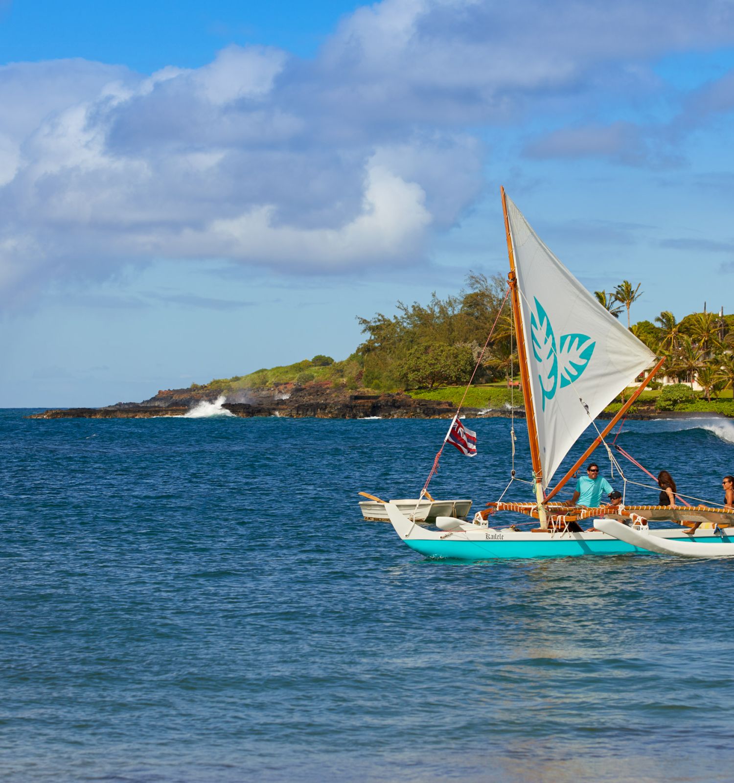 A traditional sailboat with an outrigger floats on the calm blue waters near a lush, tropical coastline under a partly cloudy sky.
