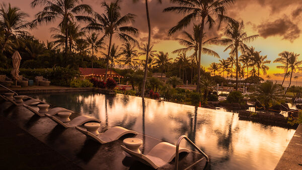 The image features a serene pool surrounded by palm trees, reflecting a beautiful sunset in a tranquil setting.