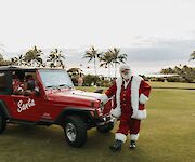 A person in a Santa outfit stands next to a red Jeep labeled 