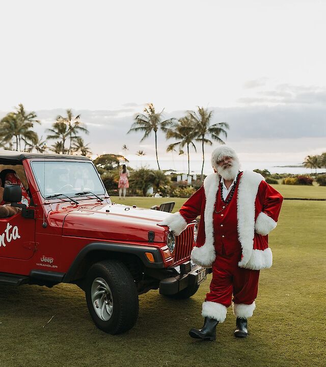 A person in a Santa outfit stands next to a red Jeep labeled 