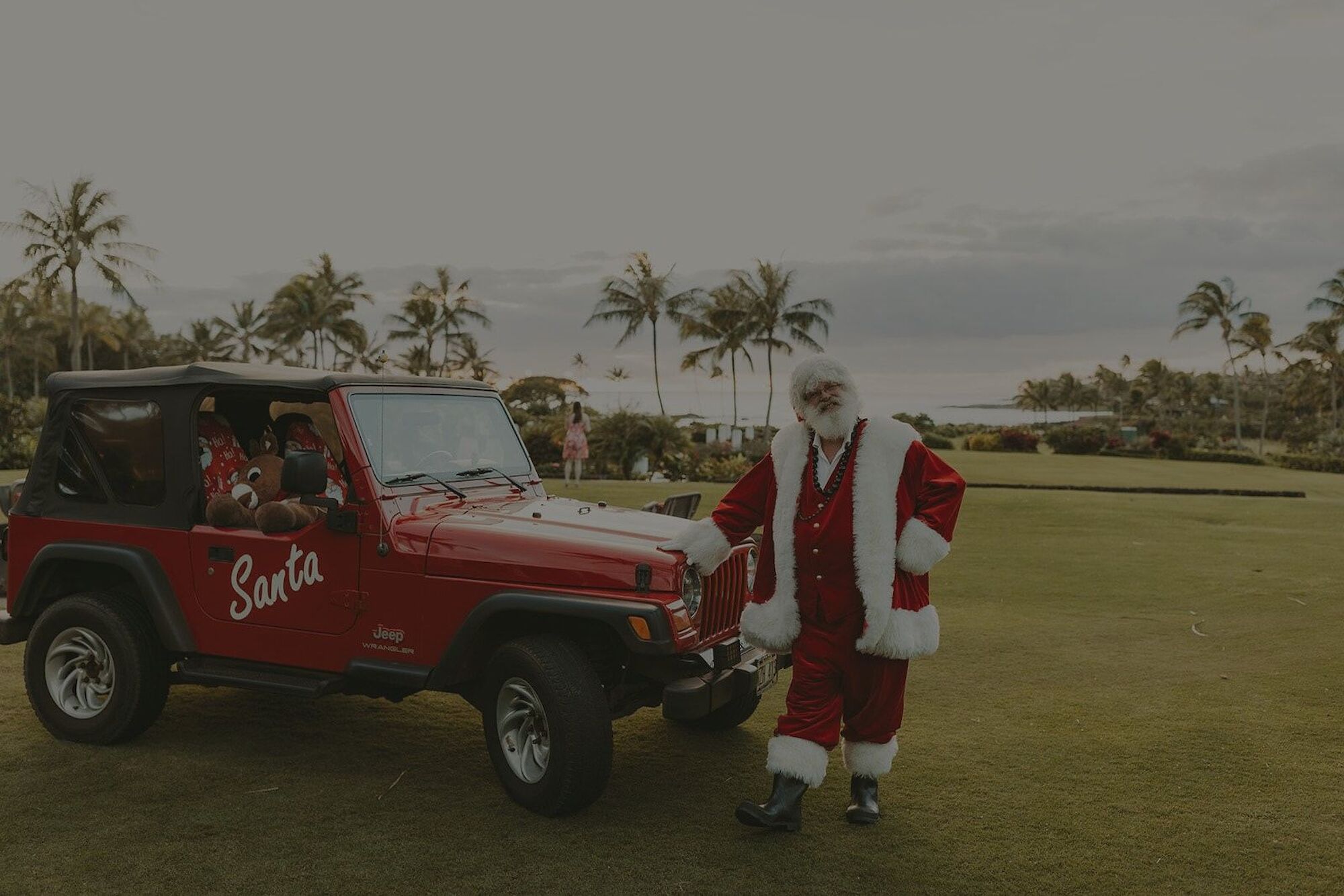The image features Santa Claus by a red Jeep, surrounded by palm trees and a scenic outdoor setting. Holiday cheer is in the air.