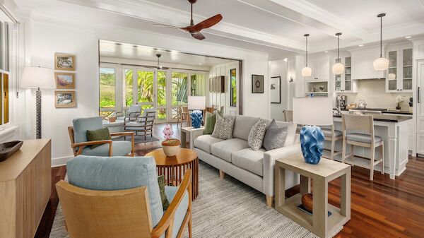 A bright, open-concept living room and kitchen with white walls, wooden floors, a gray sofa, teal chairs, a large window view, and modern decor, ending with a cozy feel.