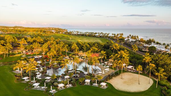 An aerial view of a tropical resort with palm trees, pools, cabanas, sandy beach, lush green lawns, and a coastline along the ocean.