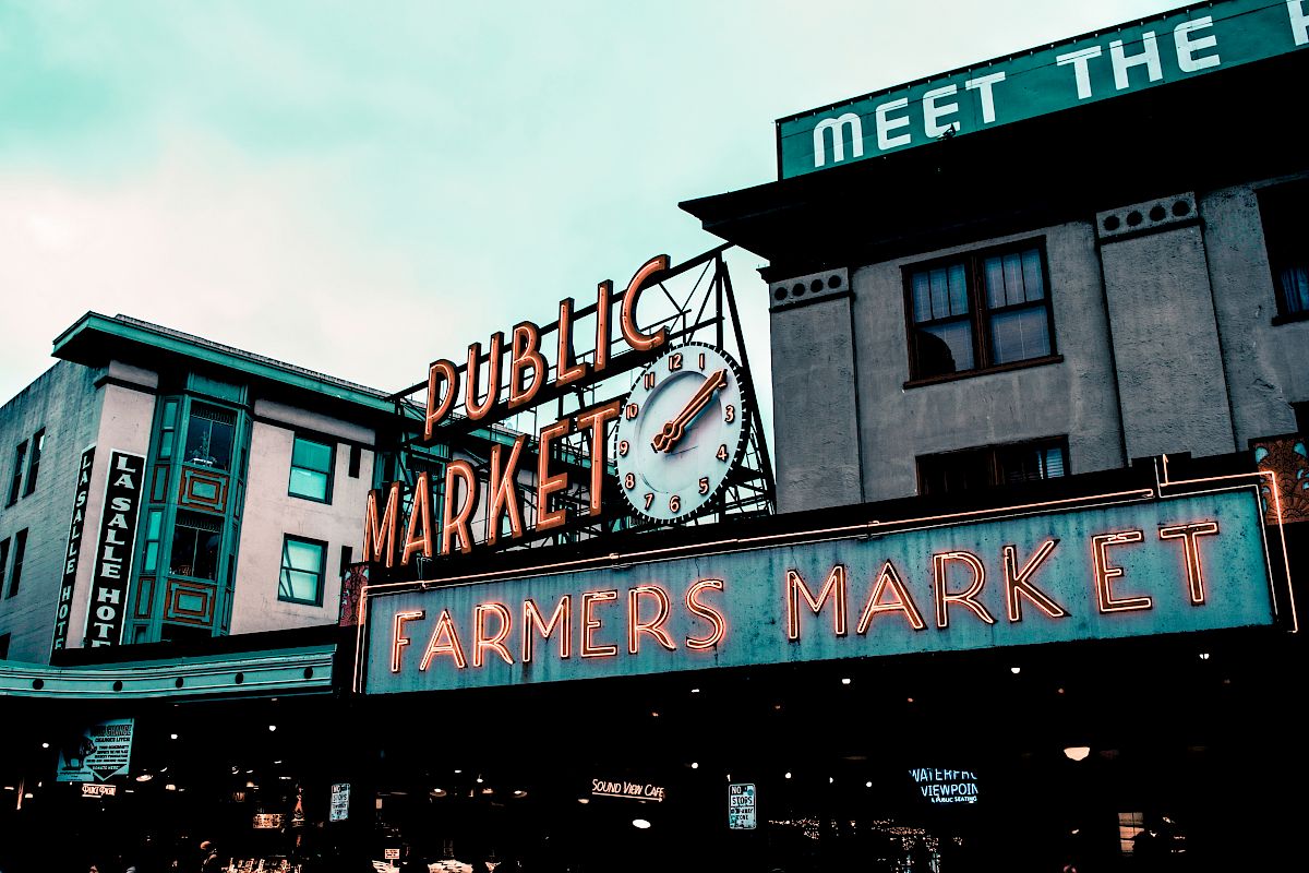 The image shows a large neon sign for a "Public Market" and "Farmers Market" on a building, with other structures visible in the background.