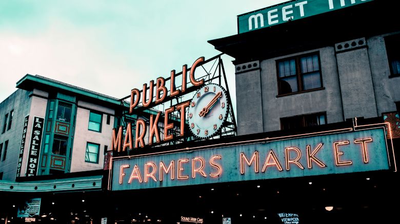 The image shows a large neon sign for a "Public Market" and "Farmers Market" on a building, with other structures visible in the background.